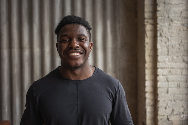 man of color smiling at camera near a brick wall
