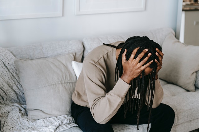 image of a man of color sitting on a couch who is crying and in distress