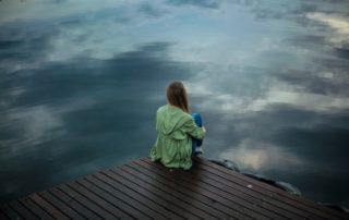 woman sitting on dock looking out at dark water