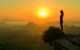 woman standing on a rock overlooking hills at sunset