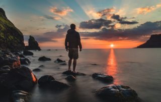 photo of a person standing on rocks that are on water overlooking sunset