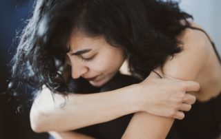 woman hugging her knees to her chest sitting on the ground