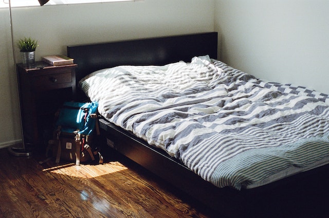 photo of a bed with a bookbag laying beside it
