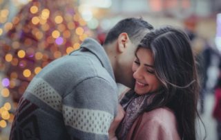 photo of a couple hugging and smiling at each other in front of a christmas tree