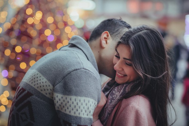 photo of a couple hugging and smiling at each other in front of a christmas tree