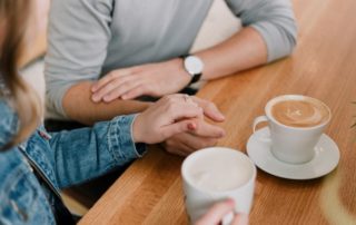photo of a couple on a date at a coffee shop with only their hands and coffee cups showing in the picture