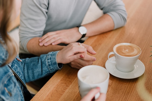 photo of a couple on a date at a coffee shop with only their hands and coffee cups showing in the picture