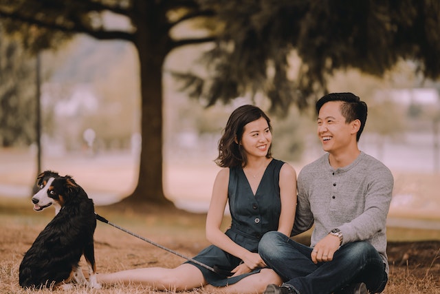 asian couple sitting in park with their dog