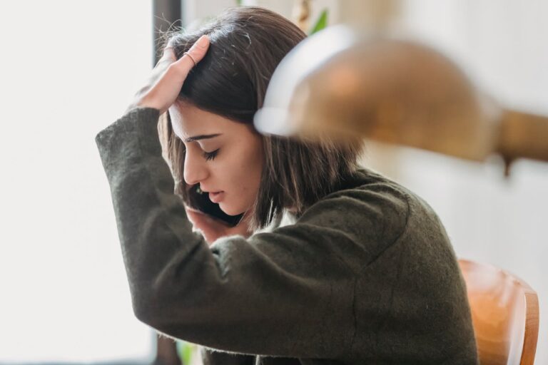 Disappointed young woman touching head while talking on smartphone