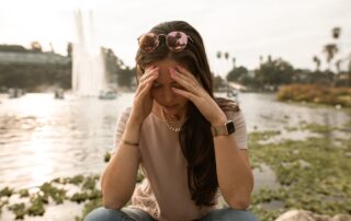 Distressed woman sitting on lakeside and touching face in despair