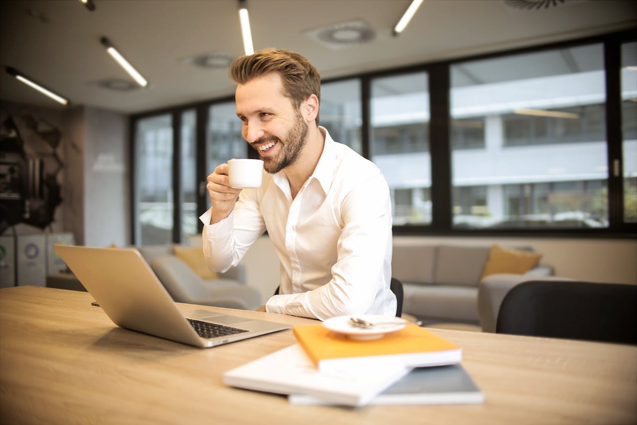 Man Sitting on Chair While Holding Cup in Front of Table 