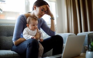 woman in front of her laptop while holding a baby