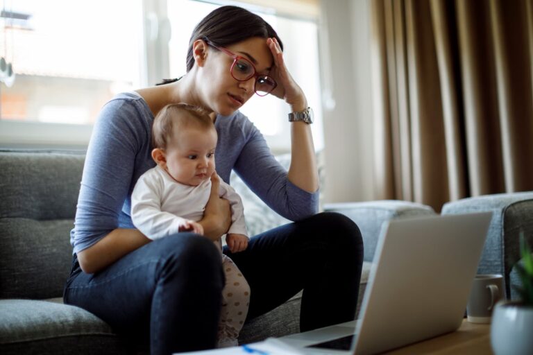 woman in front of her laptop while holding a baby