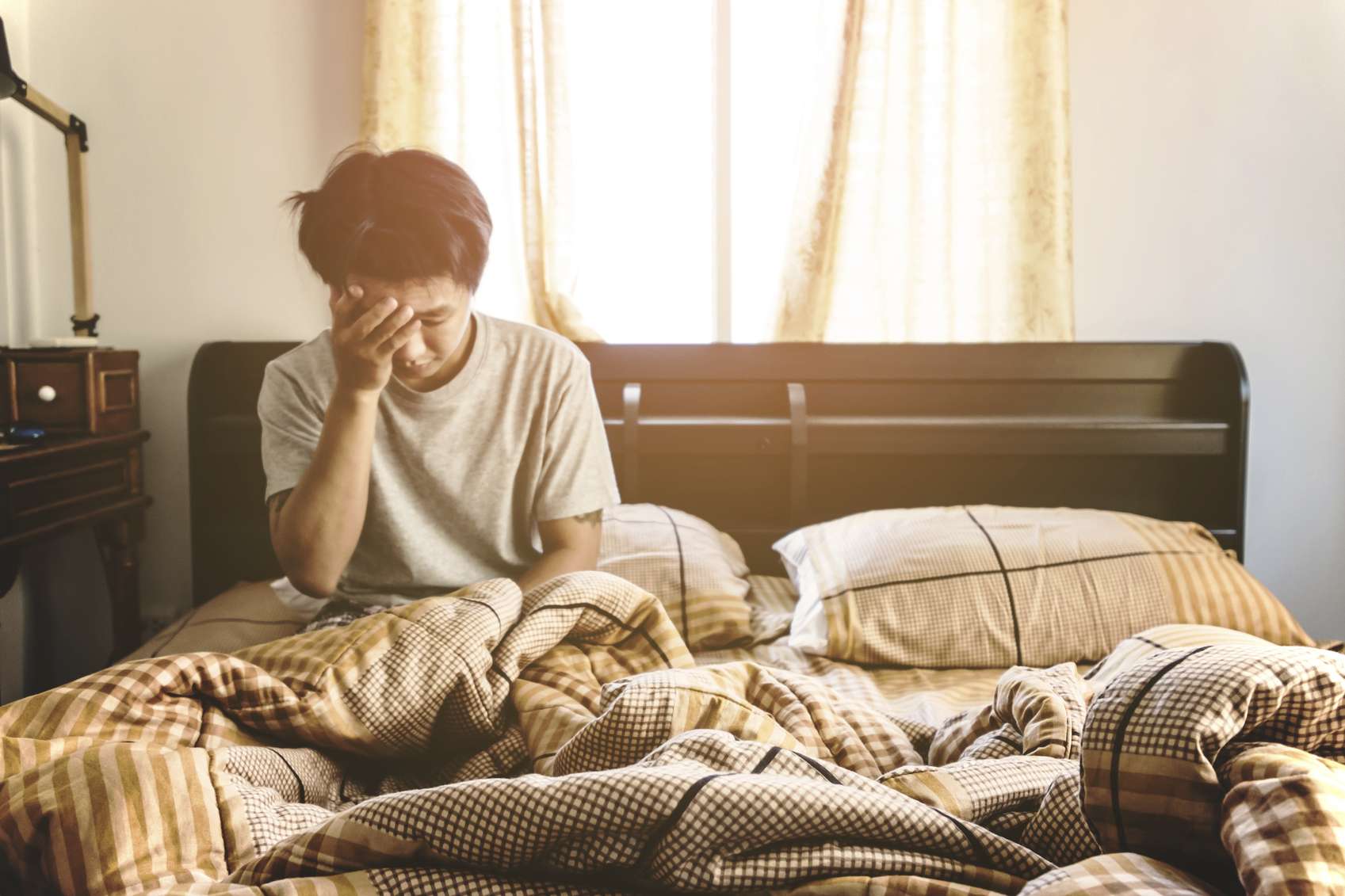 a person sitting on his bed holding his face