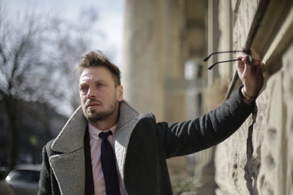 man-wearing-a-coat-holding-sunglasses