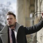 man-wearing-a-coat-holding-sunglasses