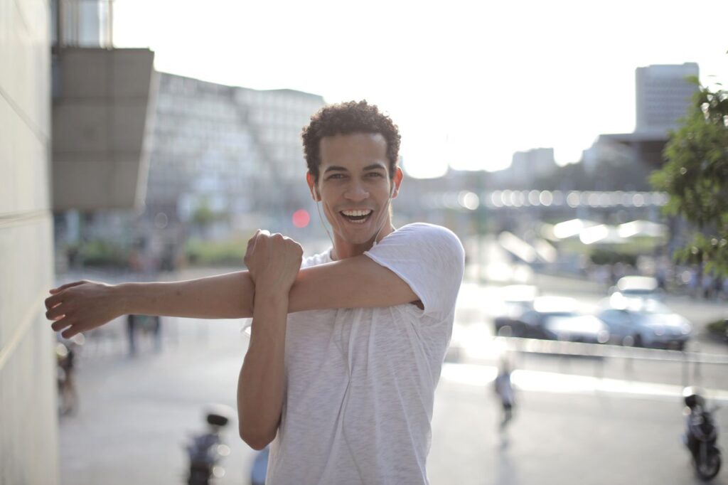 happy-young-ethnic-sportsman-stretching-arms-while-warming-up-before-training-on-street-in-city