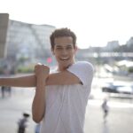 happy-young-ethnic-sportsman-stretching-arms-while-warming-up-before-training-on-street-in-city