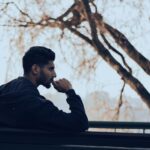 man-in-black-hoodie-sitting-on-bench-near-green-trees