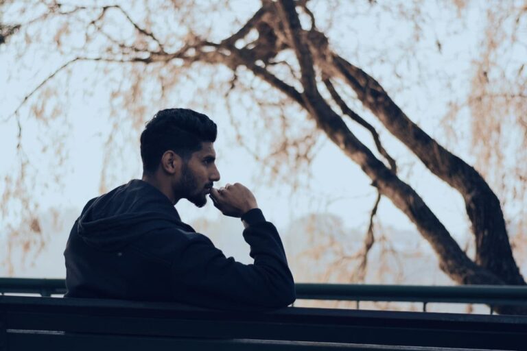 man-in-black-hoodie-sitting-on-bench-near-green-trees